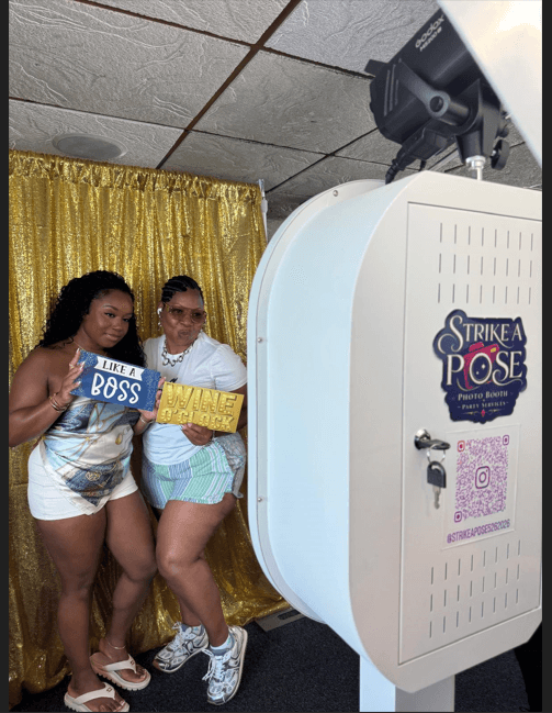 Two guests posing beside the Strike A Pose booth and gold backdrop