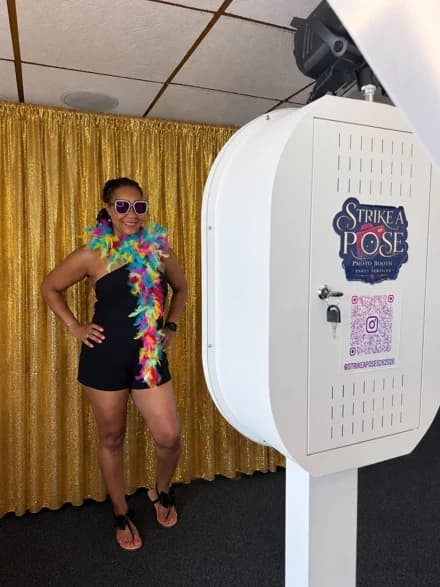 Guest posing beside the Strike A Pose Nova photo booth and gold backdrop